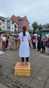 A scientist i na white lab coat gives an outdoor talk to members of the public